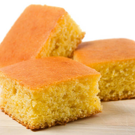 Three crumbly delicious homemade squares of melt in your mouth cornbread sitting on top of a birch cutting board.  These pieces are just begging for some sweet cream butter and clover honey to smother them.